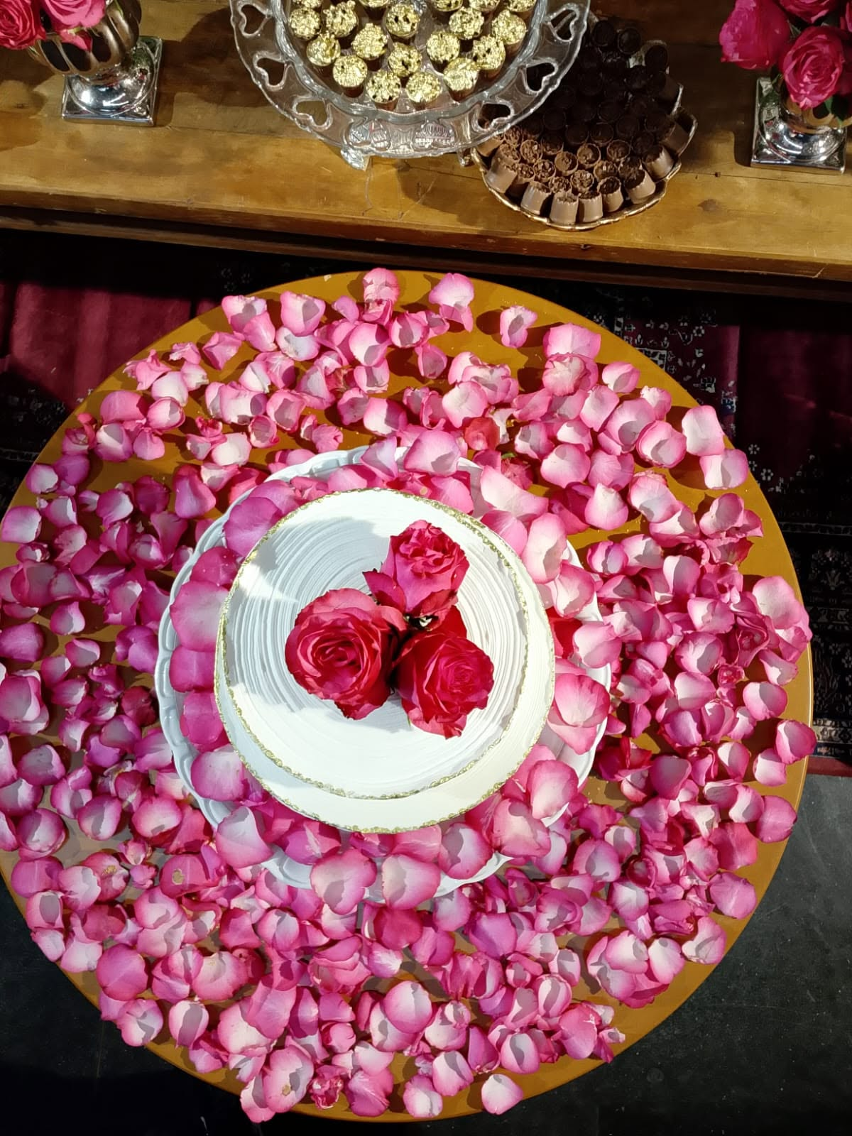 Bolo branco com rosas vermelhas sobre pétalas rosadas na mesa da festa